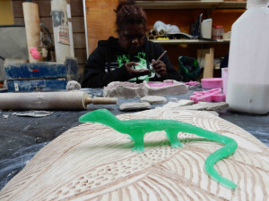 Marissa Thompson, Ngintaka sculpture in resin, with her sister Anne Thompson working on jewellery in background, Ernabella Arts, 2014, photo: Emily McCulloch Childs